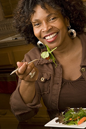 older Black woman eating salad in restaurant, smiling