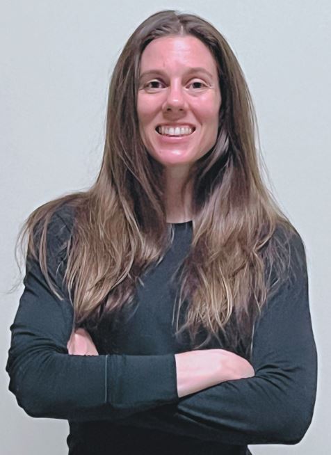 Elyse Gorrel smiling in a dark grey longsleeve, her arms cross and standing in front of a white wall