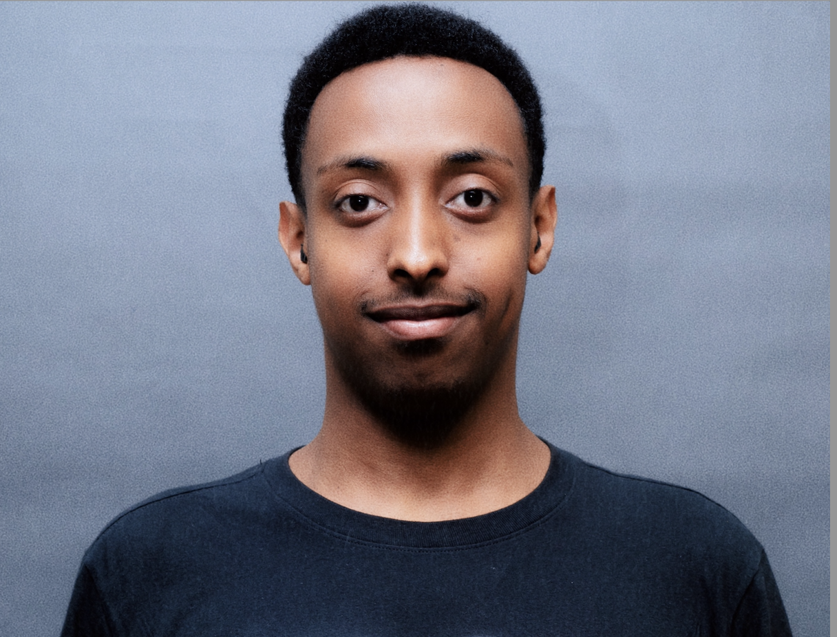 Headshot of Sami wearing a navy shirt against a grey background