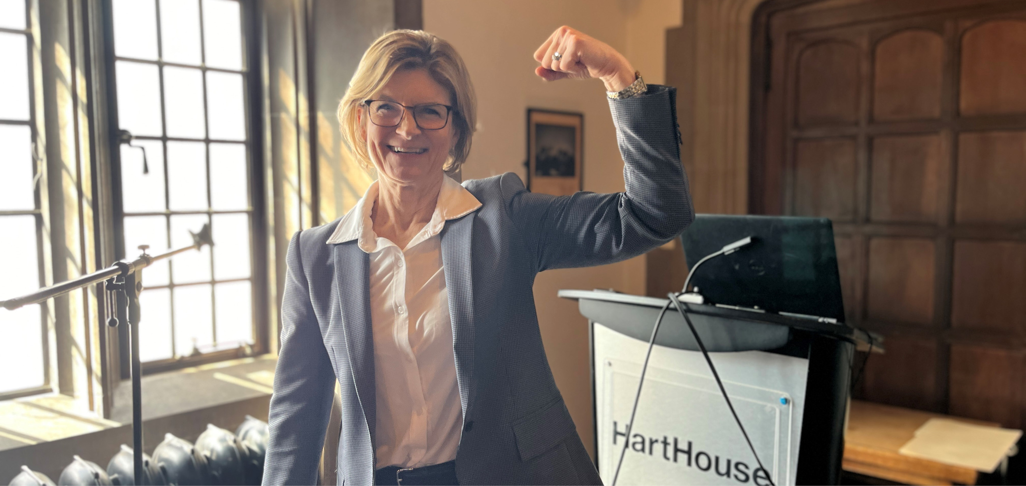 Professor Gretchen Kerr, dean of KPE, strikes a muscular pose in front of a Hart House podium