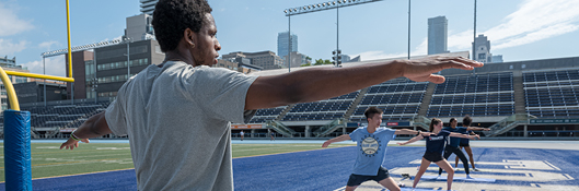 students in yoga pose on field at varsity stadium