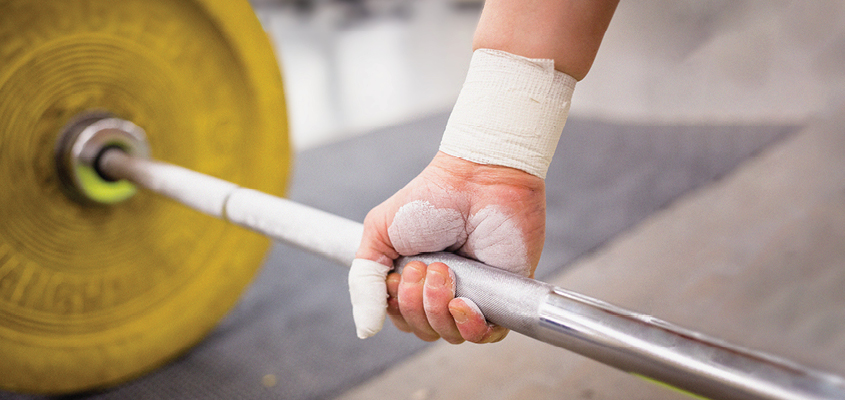 close up of chalk-covered hand gripping barbell