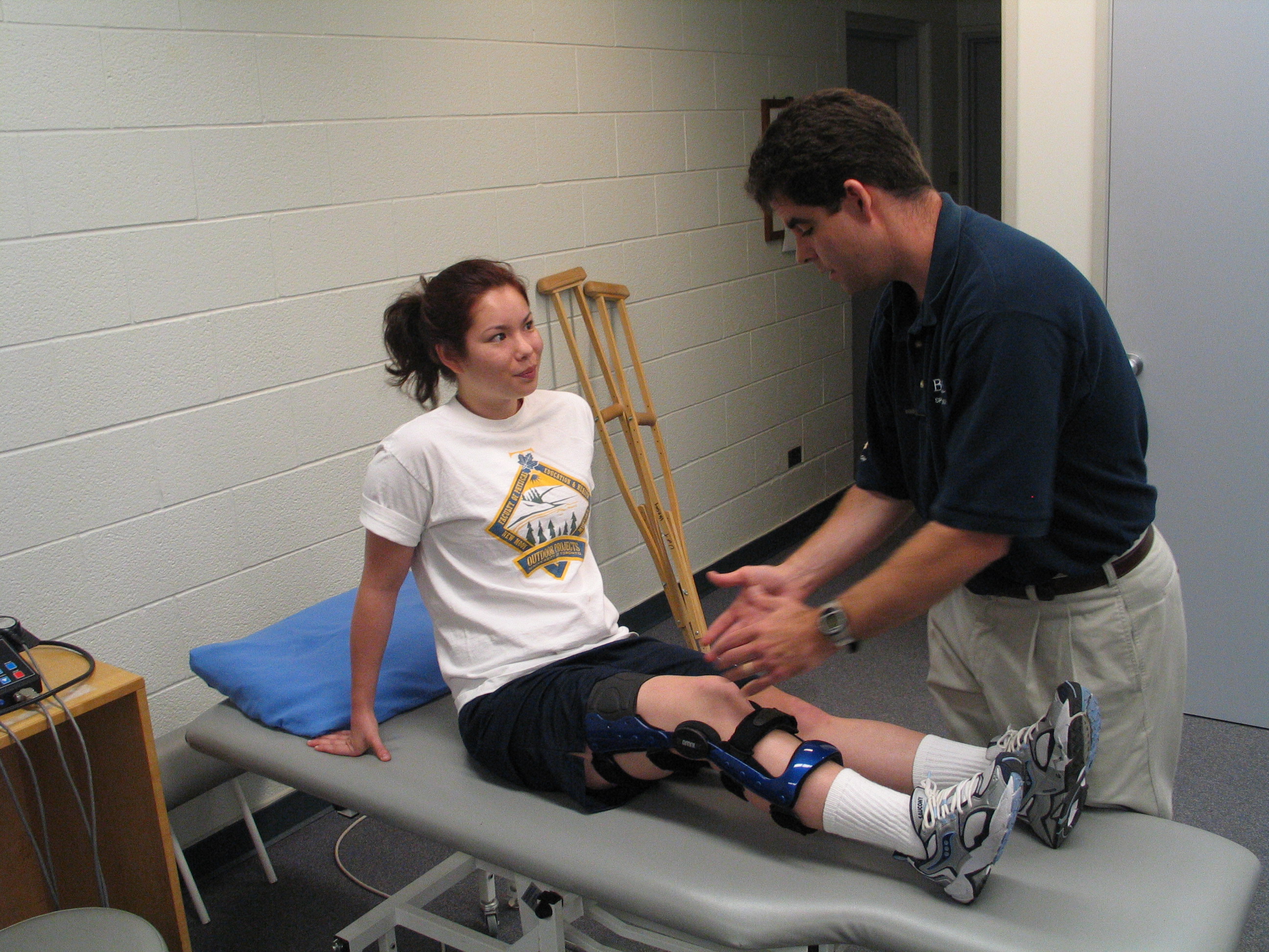 Therapist assists patient with knee brace and treatment in clinic