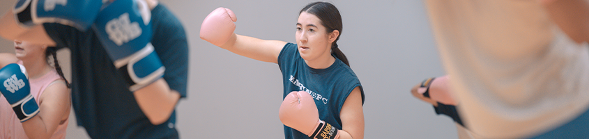 Girl boxing with a pink glove, surrounded by peers