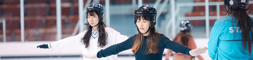 Two women with outstretched arms and helments, learning to skate