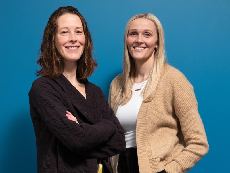 Amy Kirkham and Jenna Gillen pose for a headshot in front of a blue background