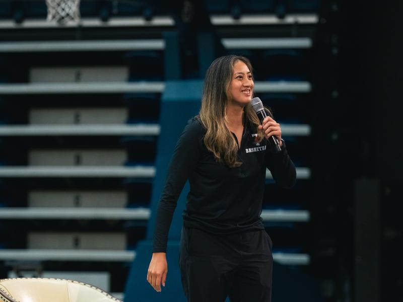 Women's basketball coach Dianna Ros smiles while holding a microphone