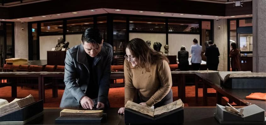 A man and a woman peruse ancient-looking texts under low light in the Fischer Rare Book Library at U of T.