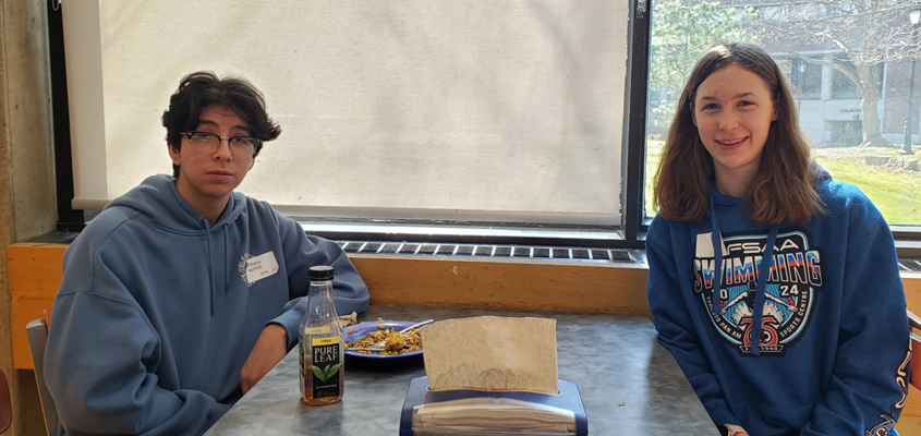 A photo of two Indigenous students at a table during lunch, smiling for the camera