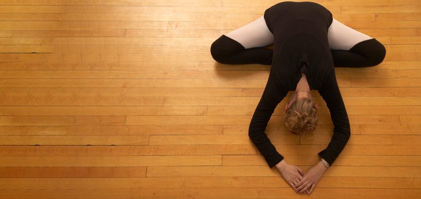 woman in ballet attire stretches on hardwood floor