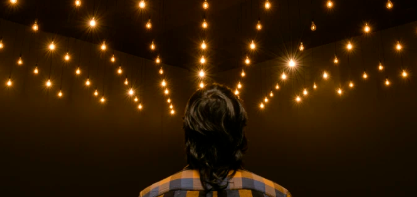 a person looks upwards at rows of suspended lightbulbs
