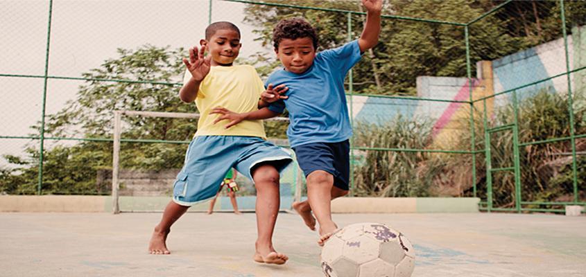 Two young children playing soccer outside.