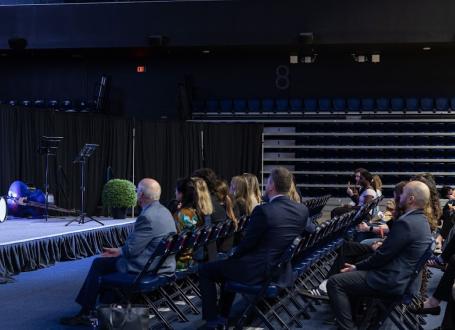 KPE Dean Gretchen Kerr addresses an audience of donors and alumni, standing on a stage in front of KPE branding in the Kimel Family Field House