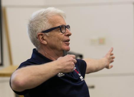 Doug Richards gestures while giving a lecture wearing a blue polo with the U of T Varsity Blues leaf logo
