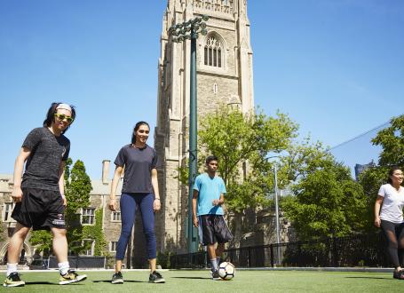 University-aged male and female students playing soccer outside on the Back Campus Fields under blue skies